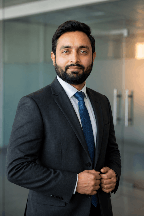 Professional headshot of Muhammad Fiaz, a freelance digital marketer and web designer, wearing a dark suit and blue tie in a modern office setting.